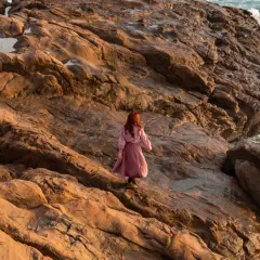 Donna con capelli rossi cammina su rocce dorate al tramonto, evocando il significato del golden hour.