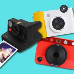 Tre moderne ai fotocamera: una Polaroid nera, una Kodak bianca e gialla, e una Leica rossa.