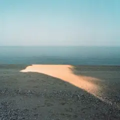Una spiaggia con un'onda di luce dorata che attraversa la sabbia, tipica di una franco fontana foto. Il mare calmo e il cielo azzurro completano la scena.