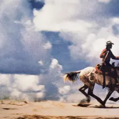Un cowboy galoppa su un cavallo bianco sotto un cielo nuvoloso. Questa è la foto più costosa al mondo.