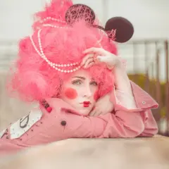 Modella con parrucca rosa shocking, trucco da clown e orecchie da topo. Un'idea per foto stravagante e colorata.