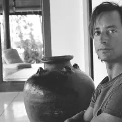 Ritratto di Herb Ritts accanto a un'antica giara, con uno scorcio di un salotto in stile tropicale sullo sfondo.