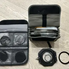 Custodia aperta con vari filtri fotografici rotondi e quadrati, un porta filtro e un anello adattatore.