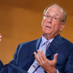 Larry Fink, il fotografo, parla con le mani. Indossa un abito blu e una cravatta a righe.