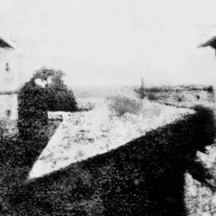 La prima foto della storia: una vista da una finestra, con figure sfocate e un paesaggio urbano lontano.