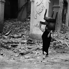 Una donna con un velo nero porta una sedia tra le macerie, un'immagine potente di resilienza catturata da David Seymour.