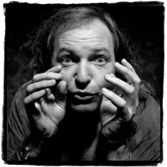 Un uomo con capelli lunghi e occhi spalancati, mani che si muovono vicino al viso. Un'espressione intensa in questa guido harari foto.