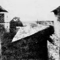 Vista sfocata di edifici e cielo, con una figura indistinta. L'atmosfera ricorda le prime fotografie di Bill Brandt.