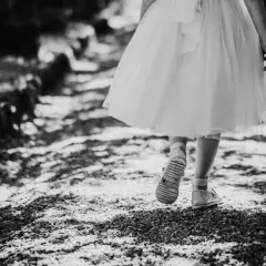 Bambina con vestito bianco cammina su un sentiero di ghiaia. Emozioni fotografie bellissime bianco e nero catturano la sua innocenza.