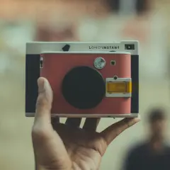Una mano tiene una Lomo'Instant. Cosa significa "fotocamera ai"? Questa fotocamera istantanea, con il suo design retrò, cattura momenti unici.