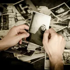 Mani che sfogliano un archivio foto, tenendo in mano una foto di una bambina. Ricordi che riaffiorano.