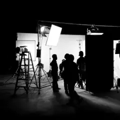 Scena di un set cinematografico con persone in silhouette, telecamere e un'intensa foto con luce.
