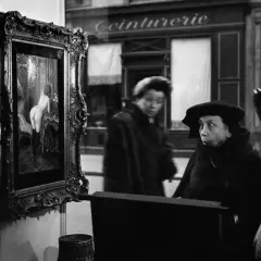Una donna guarda un quadro in una vetrina, un'altra figura sfocata sullo sfondo. Robert Doisneau foto.