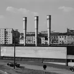 Gabriele Basilico foto: tre ciminiere svettano su un paesaggio urbano con palazzi e auto.