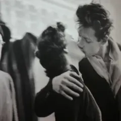 Un bacio appassionato catturato in uno degli iconici robert doisneau opere. Un uomo con berretto e occhiali osserva la scena.