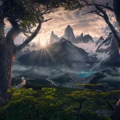 Alba dorata sui picchi innevati del **max rive**, con un lago turchese e alberi antichi in primo piano.