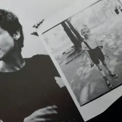 Diane Arbus, con la sua inconfondibile espressione, tiene in mano una delle sue celebri fotografie: un bambino in un parco.