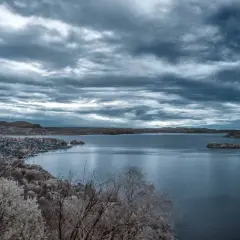 Paesaggio lacustre con cielo plumbeo, reso surreale da un filtro infrarosso fai da te che trasforma la vegetazione in bianco spettrale.