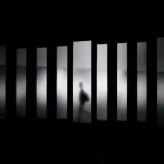 Ombra di una persona che cammina dietro pannelli verticali illuminati. Bianco e nero sono colori che creano un'atmosfera misteriosa.