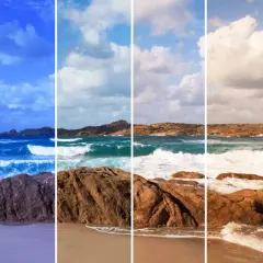 Onde che si infrangono su rocce rosse e sabbia dorata, con un cielo che sfuma dal blu intenso al bianco luminoso.