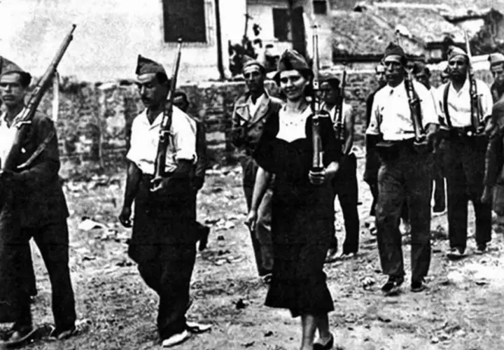 Un gruppo di miliziani marcia, tra cui una donna che ricorda Gerda Taro, con fucili in spalla.