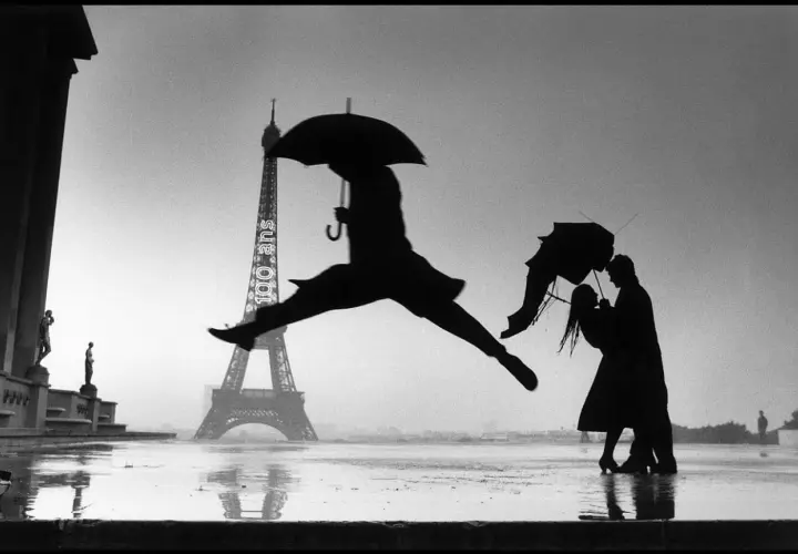Opera d'arte di Henri Cartier-Bresson: silhouette di un ballerino con ombrello salta davanti alla Torre Eiffel, mentre una coppia si abbraccia sotto un altro ombrello.