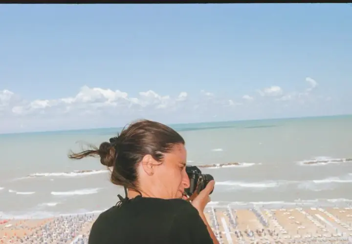 Federica Valabrega cattura la bellezza del mare con la sua macchina fotografica, mentre una spiaggia affollata si estende sotto un cielo azzurro.