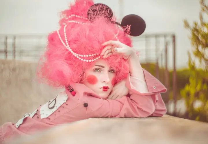 Modella con parrucca rosa shocking, trucco da clown e orecchie da topo. Un'idea per foto stravagante e colorata.