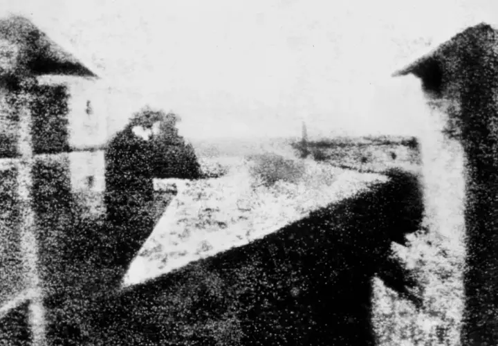 La prima foto della storia: una vista da una finestra, con figure sfocate e un paesaggio urbano lontano.