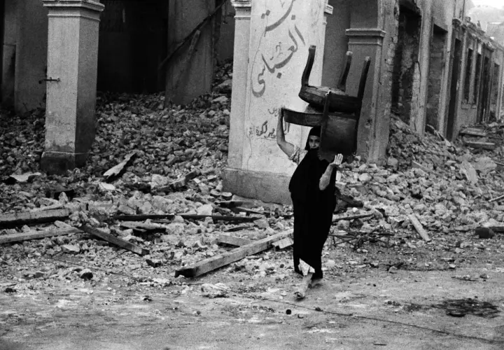 Una donna con un velo nero porta una sedia tra le macerie, un'immagine potente di resilienza catturata da David Seymour.
