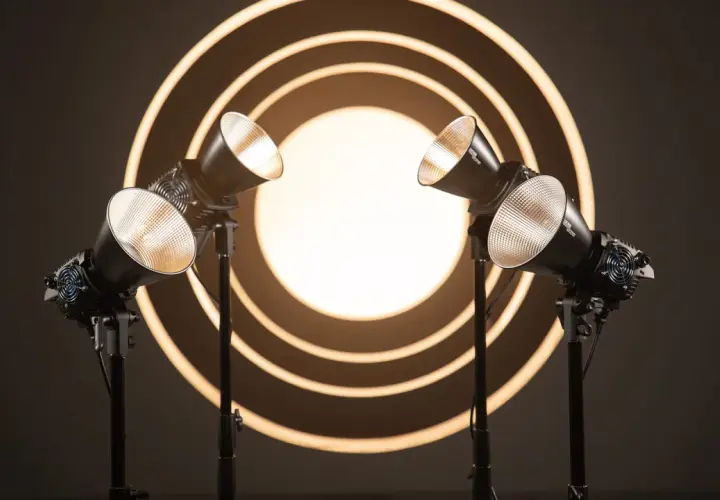 Due luci da studio creano un gioco di luce e ombra su uno sfondo con cerchi concentrici luminosi.