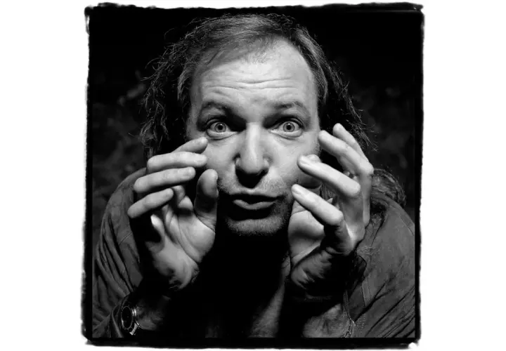 Un uomo con capelli lunghi e occhi spalancati, mani che si muovono vicino al viso. Un'espressione intensa in questa guido harari foto.