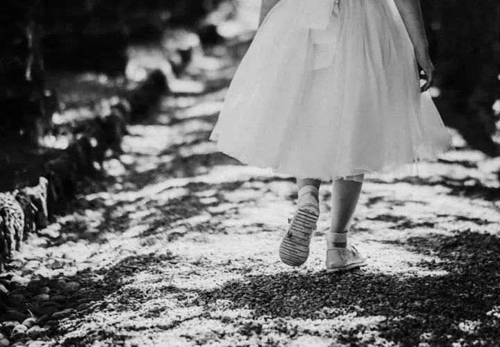Bambina con vestito bianco cammina su un sentiero di ghiaia. Emozioni fotografie bellissime bianco e nero catturano la sua innocenza.