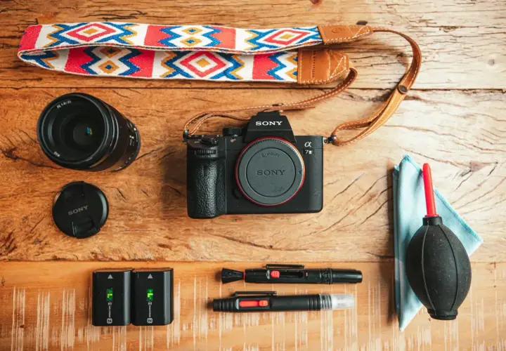Un set da fotografia flat lay: fotocamera Sony, obiettivo, batterie, cinghia colorata e accessori per la pulizia.