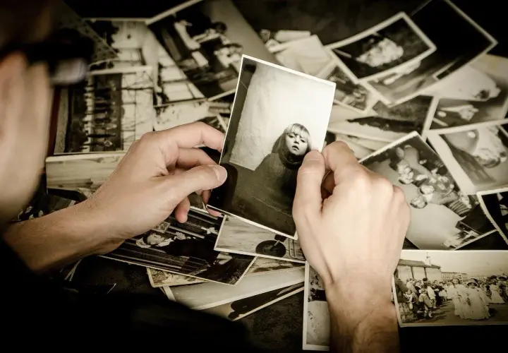 Mani che sfogliano un archivio foto, tenendo in mano una foto di una bambina. Ricordi che riaffiorano.