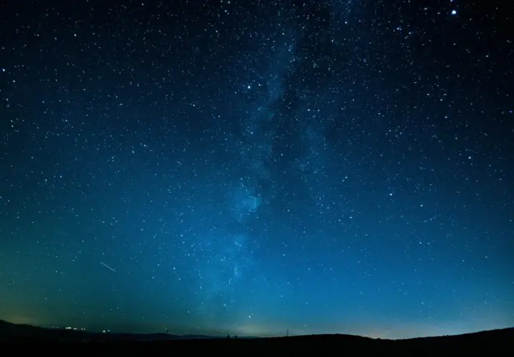 Cielo stellato blu intenso, con la Via Lattea visibile. Un'impresa di fotografare di notte a mano libera, con un leggero bagliore all'orizzonte.