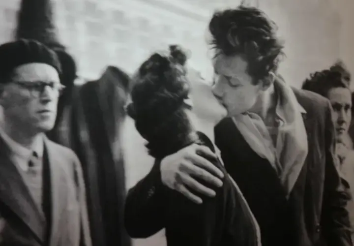Un bacio appassionato catturato in uno degli iconici robert doisneau opere. Un uomo con berretto e occhiali osserva la scena.