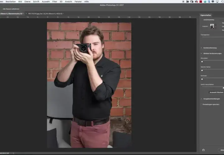 Uomo con fotocamera in mano, sullo sfondo un muro di mattoni. Interfaccia di Photoshop aperta, con pannello "Proprietà" visibile, utile per la selezione rapida Photoshop.