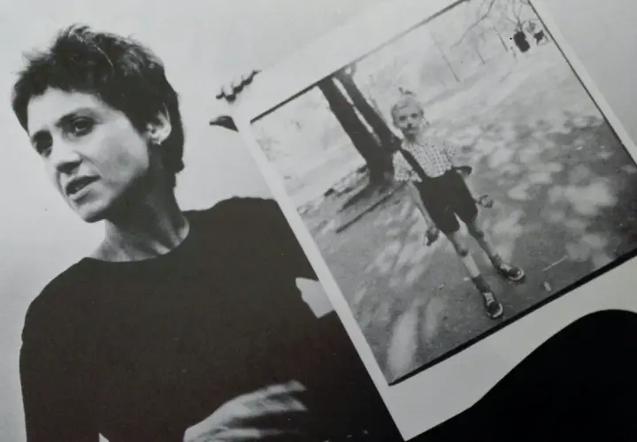 Diane Arbus, con la sua inconfondibile espressione, tiene in mano una delle sue celebri fotografie: un bambino in un parco.