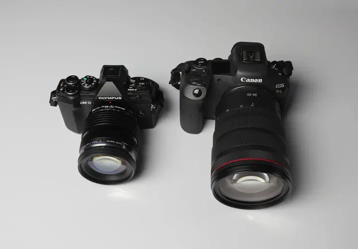 Due fotocamere, una Olympus OM-D in formato micro quattro terzi e una Canon EOS R5, affiancate su sfondo chiaro.