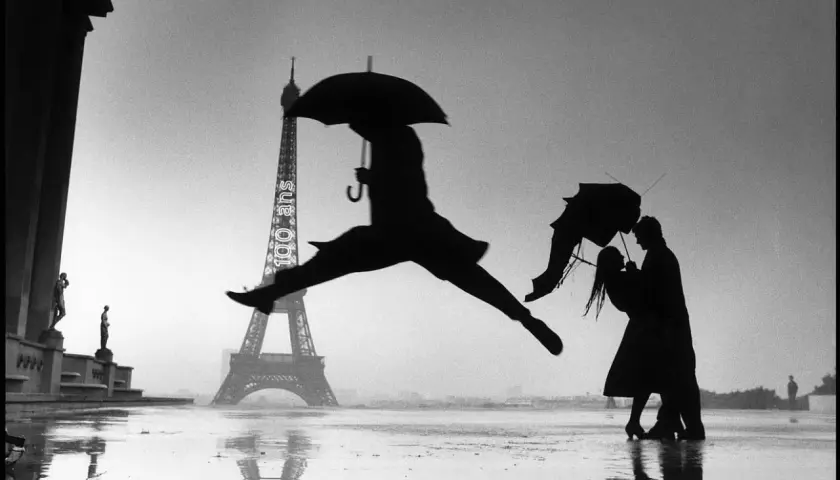Opera d'arte di Henri Cartier-Bresson: silhouette di un ballerino con ombrello salta davanti alla Torre Eiffel, mentre una coppia si abbraccia sotto un altro ombrello.