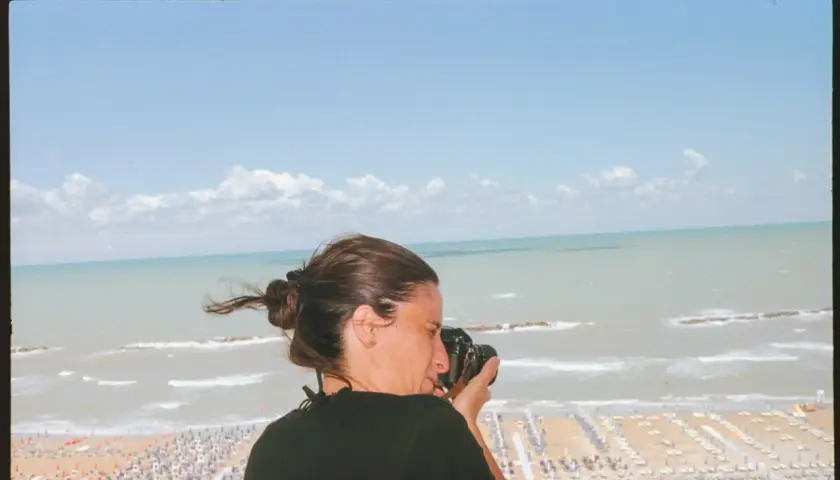 Federica Valabrega cattura la bellezza del mare con la sua macchina fotografica, mentre una spiaggia affollata si estende sotto un cielo azzurro.