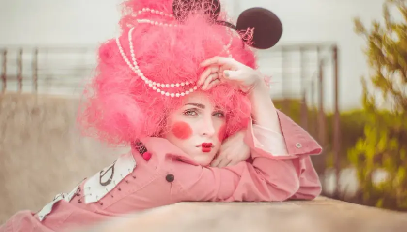 Modella con parrucca rosa shocking, trucco da clown e orecchie da topo. Un'idea per foto stravagante e colorata.