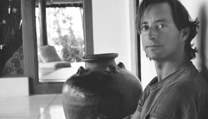 Ritratto di Herb Ritts accanto a un'antica giara, con uno scorcio di un salotto in stile tropicale sullo sfondo.