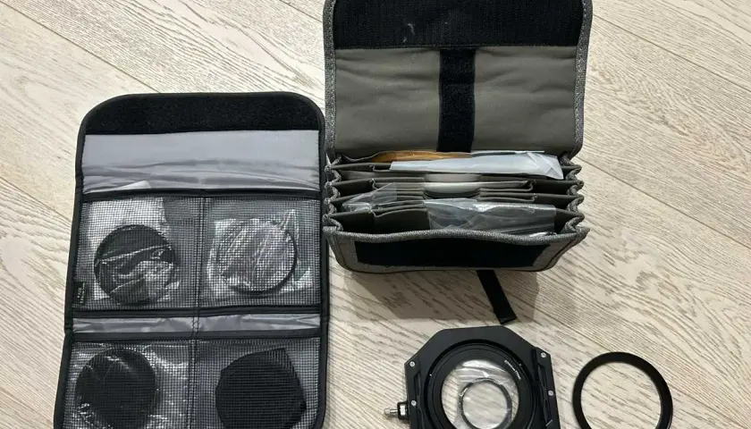 Custodia aperta con vari filtri fotografici rotondi e quadrati, un porta filtro e un anello adattatore.