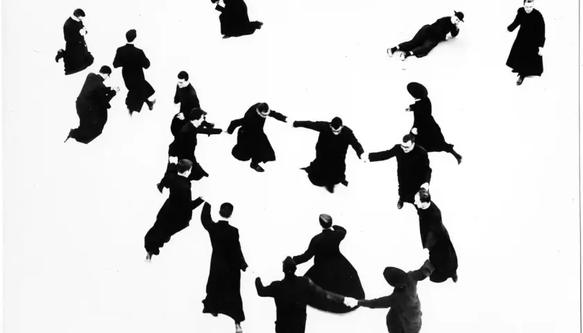 Mario Giacomelli: pretini in cerchio, alcuni in ginocchio, altri in piedi, in un gioco di ombre e forme.