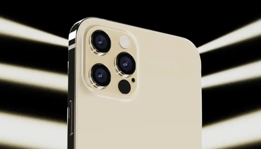 Dettaglio del modulo fotocamera dell'iPhone 12 Pro color oro, con tre obiettivi e flash, illuminato da fasci di luce su sfondo nero.