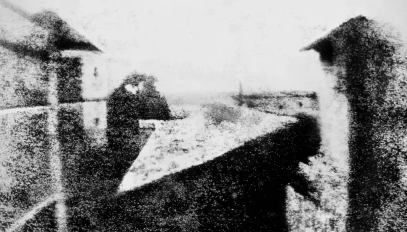 La prima foto della storia: una vista da una finestra, con figure sfocate e un paesaggio urbano lontano.