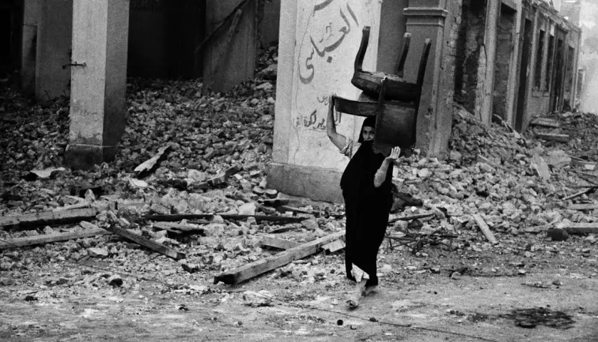 Una donna con un velo nero porta una sedia tra le macerie, un'immagine potente di resilienza catturata da David Seymour.