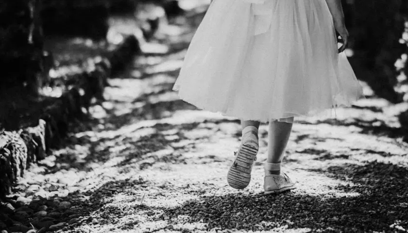 Bambina con vestito bianco cammina su un sentiero di ghiaia. Emozioni fotografie bellissime bianco e nero catturano la sua innocenza.